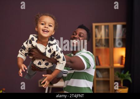 Riduci il ritratto di Happy Black father che interpreta la bambina e la tiene in aria con gioia, spazio copia Foto Stock