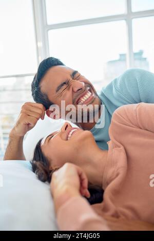 Felice giovane coppia di razza mista in una relazione amorevole ridendo mentre si rilassa a letto a casa. Fidanzato che fa una faccia stupida mentre lo dice Foto Stock