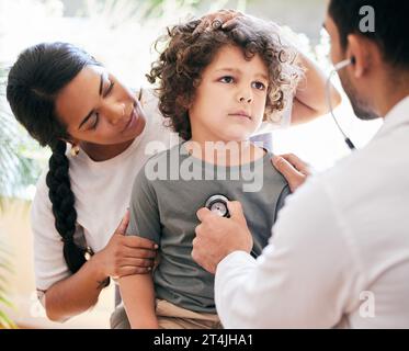 Per favore, lo renda migliore. un bambino che viene esaminato da un medico irriconoscibile mentre sua madre lo tiene. Foto Stock