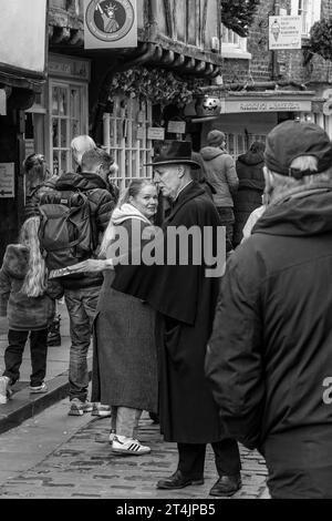 I volantini per la Ghost Walk vengono distribuiti da un anziano gentiluomo vestito di nero pieno e un cappello da bowling lungo la Shambles a York, Regno Unito. Foto Stock