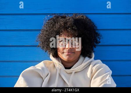 Donna nera vestita con felpa berretto e capelli afro su sfondo blu in una giornata di sole Foto Stock