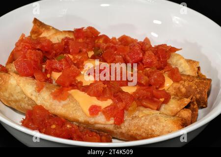 Flautas in un recipiente bianco ricoperto di formaggio e salsa. Foto Stock