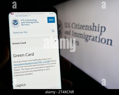 Persona che possiede un telefono cellulare con una pagina Web dell'agenzia statunitense Citizenship and Immigration Services (USCIS) con sigillo. Concentrarsi sul centro del display del telefono. Foto Stock