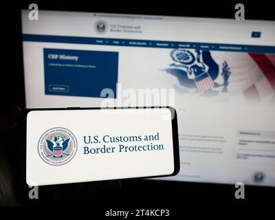 Persona che possiede uno smartphone con il sigillo dell'agenzia United States Customs and Border Protection (CBP) davanti al sito Web. Concentrarsi sul display del telefono. Foto Stock