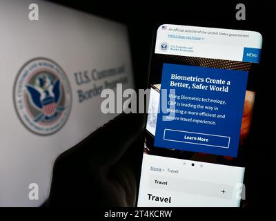 Persona in possesso di cellulare con pagina web dell'agenzia United States Customs and Border Protection (CBP) con sigillo. Concentrarsi sul centro del display del telefono. Foto Stock