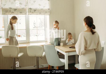 i bambini mangiano cibo sano a casa, la mamma li guarda Foto Stock