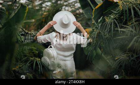 Vista posteriore di una botanica donna vestita in stile safari in piedi nella serra di palme del giardino botanico Foto Stock
