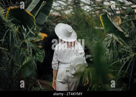 Vista posteriore di una botanica donna vestita in stile safari in piedi nella serra di palme del giardino botanico Foto Stock