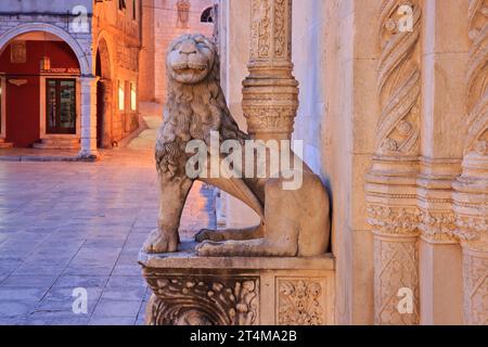 Una statua di leone splendidamente scolpita a guardia dell'ingresso laterale della cattedrale di San Giacomo (1431-1535) all'alba a Sibenik, Croazia Foto Stock