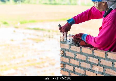 Mano ravvicinata del muratore che installa mattoni in cantiere. Foto Stock