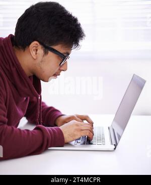 Svolgere l'attività in modo efficiente. un bel giovane che lavora al suo portatile in un ufficio. Foto Stock