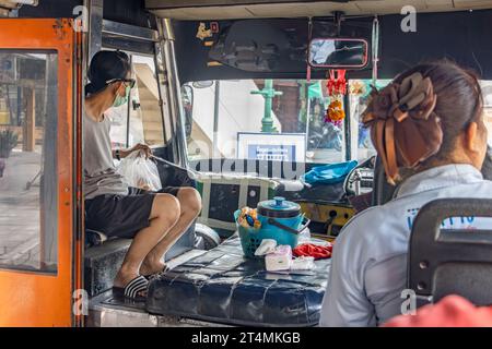 BANGKOK, THAILANDIA, ottobre 28 2023, Un passeggero siede sopra il motore di fronte a un vecchio autobus cittadino Foto Stock