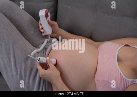 Primo piano della pancia di una donna incinta usando un doppler domestico. Schermo vuoto. Foto Stock