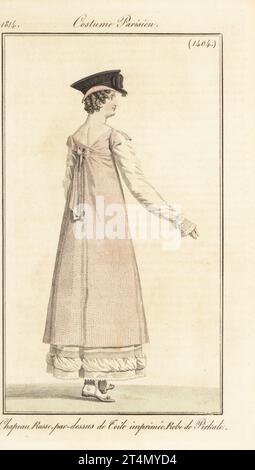 Donna alla moda con berretto russo nero, tunica stampata su un abito in cotone percale. Chapeau russe, par-dessus de toile imprimee, robe de Perkale. Incisione a mano su copperplate di Jean Charles Baquoy dopo un piatto di moda di Horace Vernet dal Journal des Dames et des Modes di Pierre de la Mesangere, Magazine of Women and Fashion, Parigi, 1814. Foto Stock