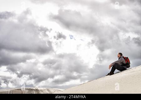 Godendo della solitudine. un affascinante escursionista maschile seduto sulle dune di sabbia. Foto Stock