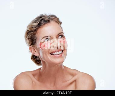 Vedrai i risultati velocemente. una donna matura che indossa cerotti in gel sotto gli occhi mentre posa su uno sfondo bianco. Foto Stock