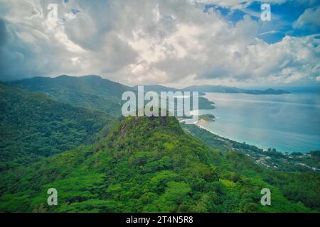 Shot di drone dalla fabbrica di tè, vista da sud-ovest alla costa occidentale di Mahe dietro mont Sephale, cielo nuvoloso, Mahe Seychelles Foto Stock