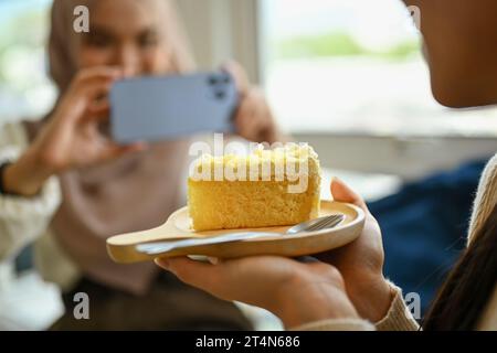 Immagine ritagliata di una giovane donna che tiene un piatto di torta e di un suo amico che scatta foto con lo smartphone Foto Stock