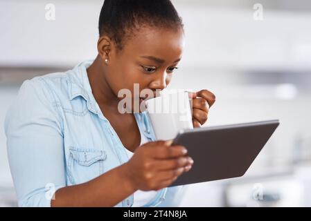 Versare un po' di tè sui social media. una donna che beve caffè mentre usa un tablet digitale a casa. Foto Stock