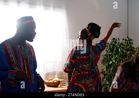 Giovane donna afroamericana in abbigliamento etnico che tiene il braccio alzato durante la danza mentre si trova accanto al marito indossando costume nazionale Foto Stock