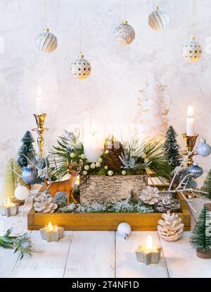 Composizione natalizia di candele, cervi, coni di pino, baule natalizie, rami di abete, fiori, muschio, bacche invernali in scatola di legno. Accogliente camera invernale Foto Stock