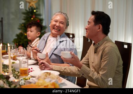 Donna anziana che ride quando parla con suo figlio adulto a cena di famiglia Foto Stock