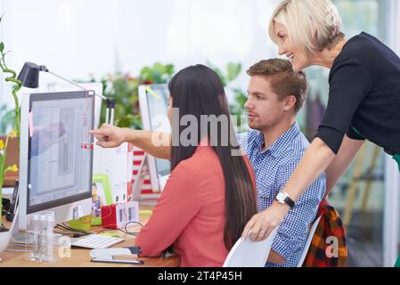 Cosa ne pensi di questo? Un giovane uomo d'affari che mostra qualcosa a due colleghi donne sul suo computer. Foto Stock