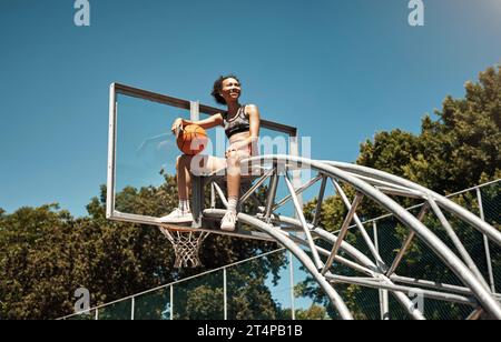 Hai quello che serve per diventare il migliore? una giovane donna sportiva seduta su un canestro da basket su un campo sportivo. Foto Stock