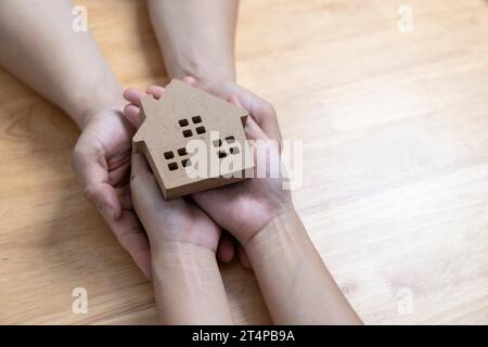 mani che tengono la casa di legno, casa di famiglia, crisi abitativa senza tetto, depressione economica, concetto di mutuo Foto Stock