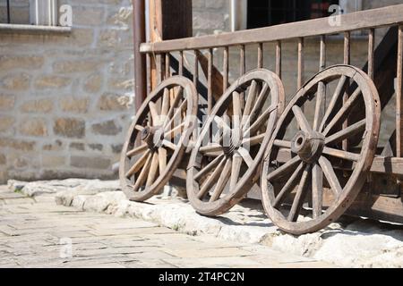 Tre vecchie ruote in legno per carri trainati da cavalli appoggiati in prospettiva a un muro di legno Foto Stock