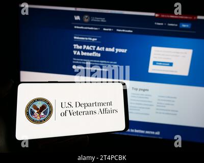 Persona che possiede un telefono cellulare con il sigillo del Dipartimento dei Veterani degli Stati Uniti (va) davanti alla pagina Web. Concentrarsi sul display del telefono. Foto Stock