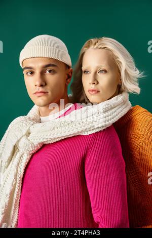 giovane coppia che indossa maglioni che condividono la sciarpa bianca e si posa insieme su un turchese alla moda invernale Foto Stock