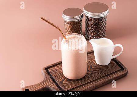 Frullato o caffè appena fatto con latte in un moderno bicchiere a forma di barattolo di birra su un tagliere di legno. Vista frontale Foto Stock