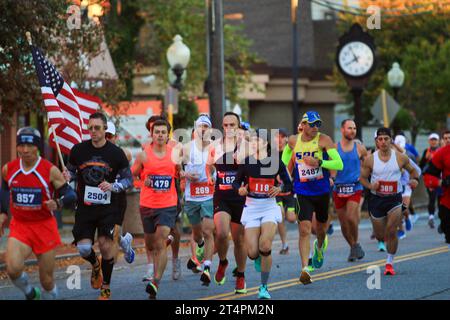 Babylon, New York, USA - 22 ottobre 2023: Uomo che porta la bandiera americana all'inizio di una maratona che corre in una corona di corridori attraverso Babylon Vill Foto Stock