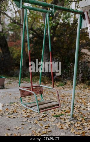 Un vecchio altalena su un parco giochi per bambini realizzato con struttura metallica. Elementi di gioco non sicuri obsoleti. Cortile sovietico nel fogliame autunnale Foto Stock