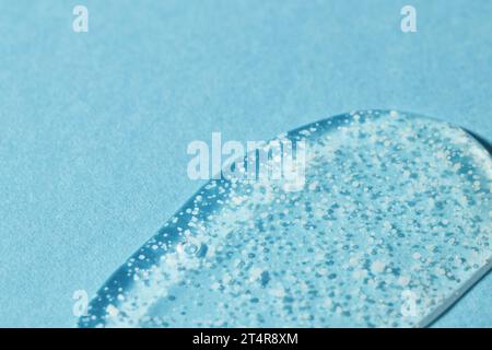 Goccia di gel di lavaggio scrub su sfondo blu per levigare. Gel liquido trasparente con perle lucidanti per un'esfoliazione delicata in primo piano. Foto Stock