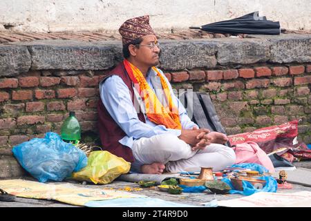 Kathmandu, Nepal: Guru indù in attesa che una famiglia prepari regali per i morti al tempio Pashupatinath, famoso tempio indù dedicato a Shiva Foto Stock