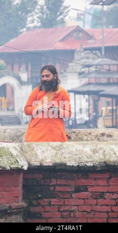 Kathmandu, Nepal: Guru indù in attesa che una famiglia prepari regali per i morti al tempio Pashupatinath, famoso tempio indù dedicato a Shiva Foto Stock