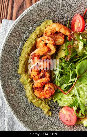 Gamberetti grigliati serviti con pesto, mix di insalate, zucchine grigliate e pomodori ciliegini freschi in un recipiente grigio. Foto Stock