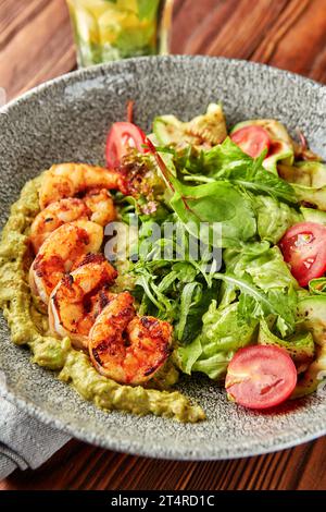 Gamberetti grigliati serviti con pesto, mix di insalate, zucchine grigliate e pomodori ciliegini freschi in un recipiente grigio. Foto Stock