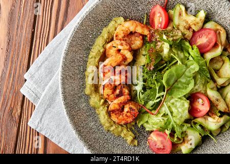 Gamberetti grigliati serviti con pesto, mix di insalate, zucchine grigliate e pomodori ciliegini freschi in un recipiente grigio. Foto Stock