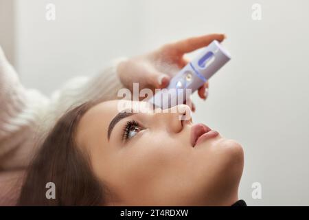 cosmetologo che utilizza primer spray per la procedura di estensione delle ciglia in salone Foto Stock