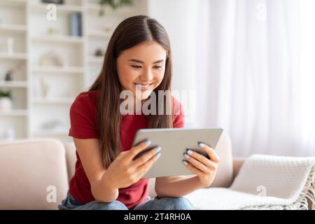 Una giovane donna asiatica sorridente che si rilassa con un tablet digitale a casa Foto Stock