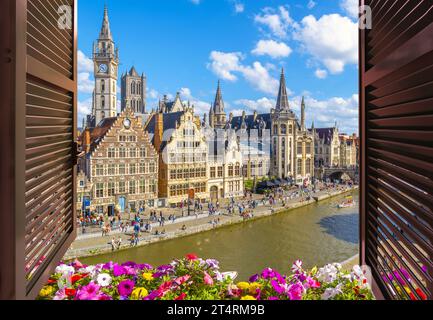 Vista attraverso una finestra aperta con persiane e scatola di fiori di caffetterie e negozi nel quartiere medievale di Graslei sul fiume Leie, a Gand, in Belgio. Foto Stock