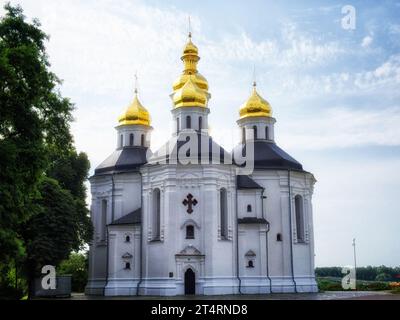 Una chiesa bianca con cupole e croci dorate, incastonata tra lussureggiante vegetazione sotto un cielo blu con nuvole. Splendido cielo sopra la Chiesa ortodossa di San Foto Stock