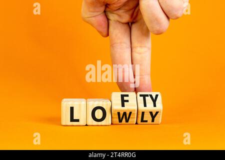 Simbolo alto o basso. Parole concettuali Lofty lowly su blocco di legno. Bellissimo sfondo arancione. Mano d'affari. Affari alti o bassi Foto Stock