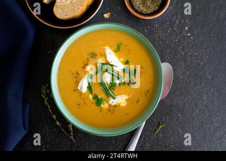 Zuppa di zucca con panna fresca ed erbe preparate dall'alto su uno sfondo di ardesia scura Foto Stock