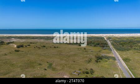 Vista dall'alto del kijkduin della spiaggia e del mare. Sorvola i campi con erba verde ed edifici sulla riva del mare. Tetti di case sullo sfondo. Visualizza da Foto Stock