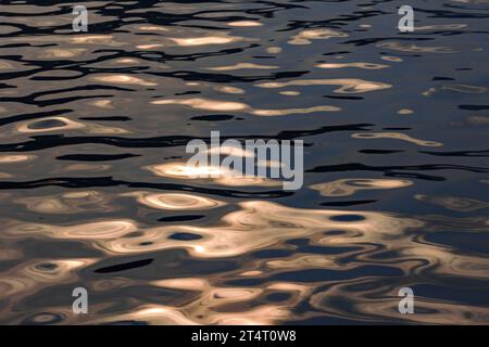 Ondulazioni d'acqua e onde riflettono il sole estivo reso nebbioso e scuro dal fumo di fuoco selvatico sull'oceano a Vancouver, Canada. Motivi e forme arancioni. Foto Stock