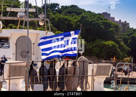 La bandiera nazionale greca su un albero sbatte sullo sfondo del cielo blu e della vecchia fortezza di Rodi. Grecia. Foto Stock